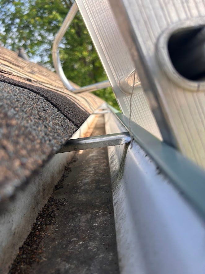 Close-up of a ladder leaning against a roof gutter covered in debris and leaves.