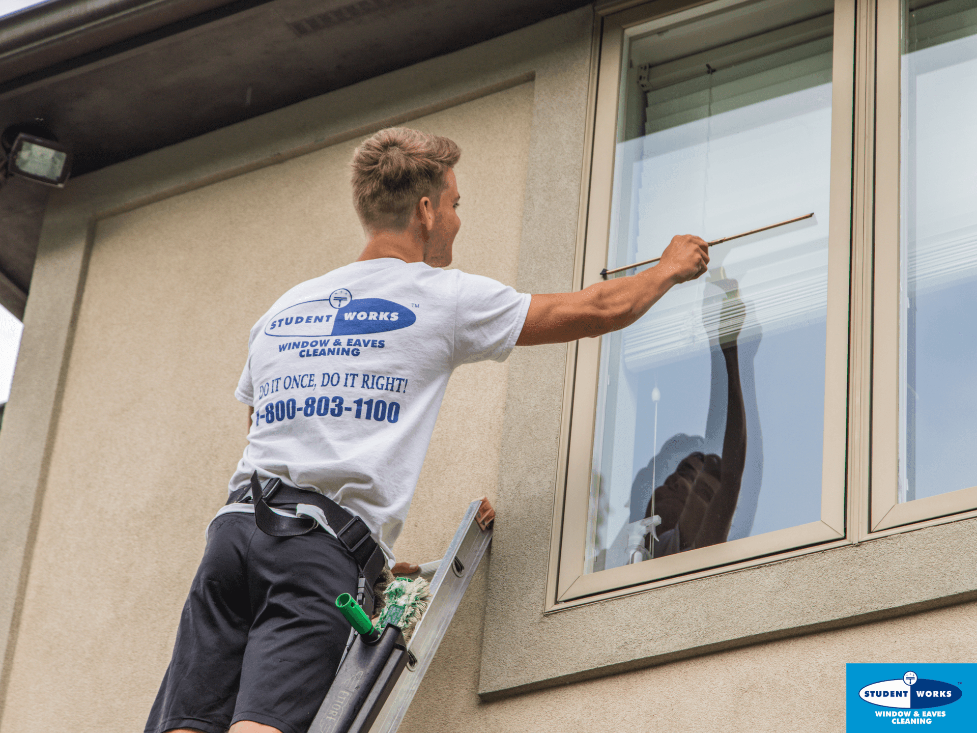 Worker on a ladder cleaning a second-story window while wearing a 'Student Works' uniform.